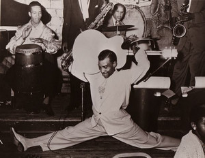 Black and white performance photo of T-Bone Walker doing a split while playing electric guitar onstage.