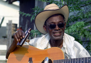 Outdoor photograph of Lightnin' Hopkins in a cowboy hat leaning on an acoustic guitar.