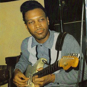 Junior Wells singing into a microphone in a club with a guitar visible behind him.