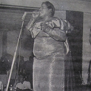 Big Mama Thornton singing into a microphone onstage in a formal dress.