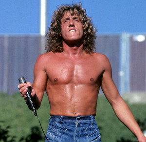 Roger Daltrey shirtless at Woodstock, gripping a microphone and looking upward.