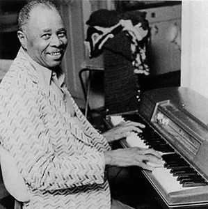 Floyd Dixon smiling at a piano in a patterned jacket.