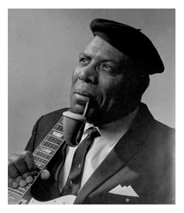 Albert King in a studio portrait wearing a beret and smoking a pipe beside a guitar neck.