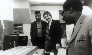 Muddy Waters, Marshall Chess, and Charles Stepney gathered around a recording console in a studio.