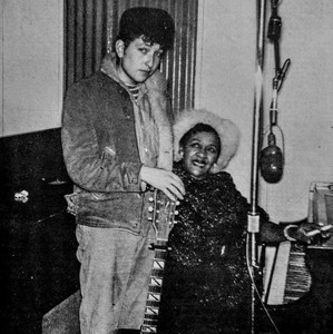 Bob Dylan standing with guitar beside seated Victoria Spivey at a piano.