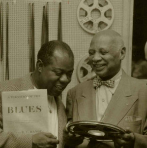 Louis Armstrong and W.C. Handy smiling together in a recording studio.