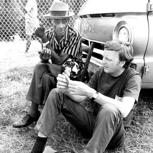 Mance Lipscomb seated outdoors beside Chris Strachwitz near a parked van.
